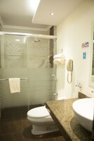 Un baño moderno con ducha envuelta en vidrio, inodoro blanco y encimera de granito con lavamanos.