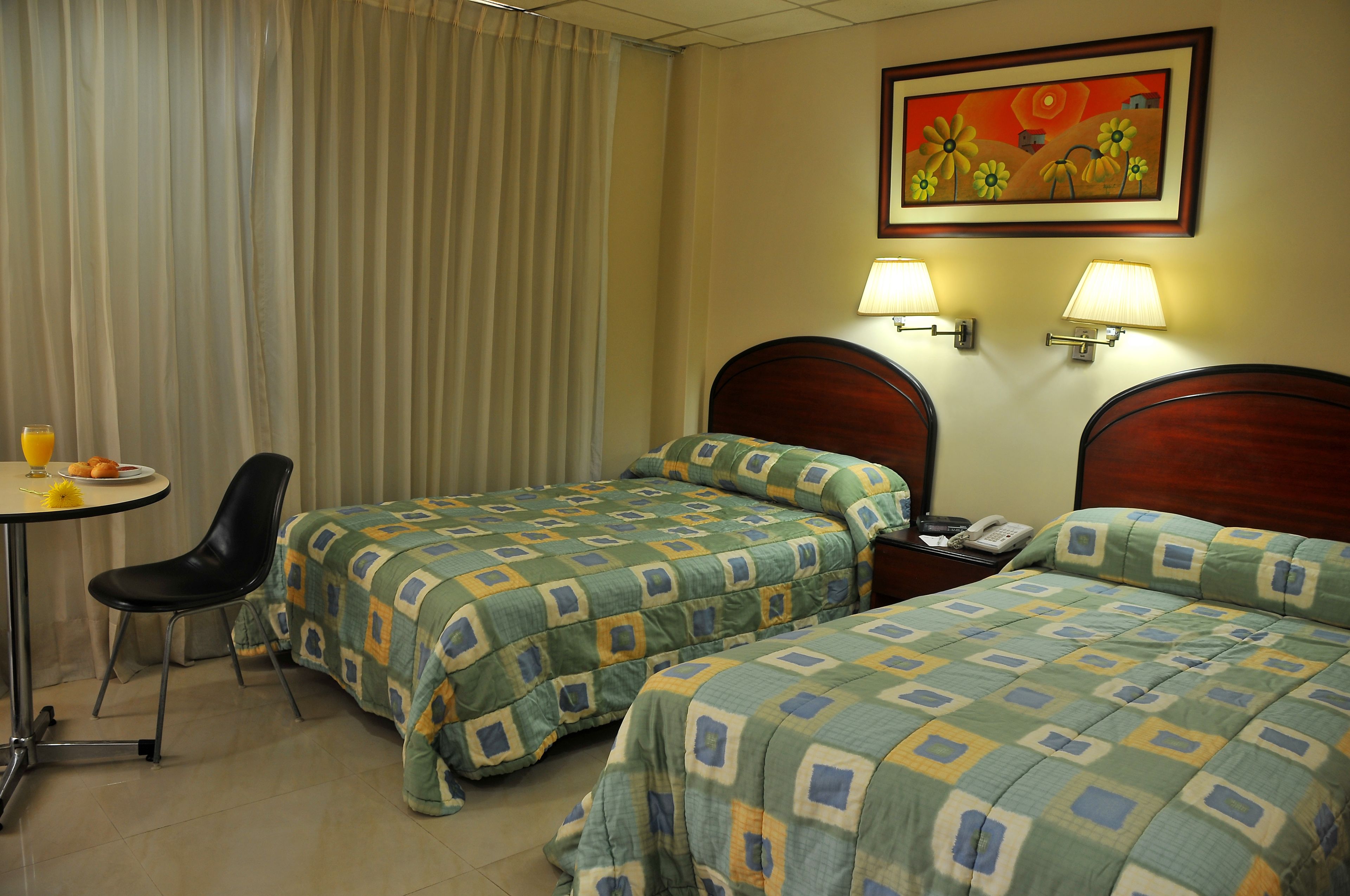 Habitación de hotel con dos camas individuales, una mesita con una silla, un teléfono y un cuadro en la pared.
