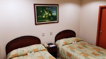 Un dormitorio con dos camas individuales, una mesita de noche con un teléfono y un libro, un cuadro en la pared y una puerta.