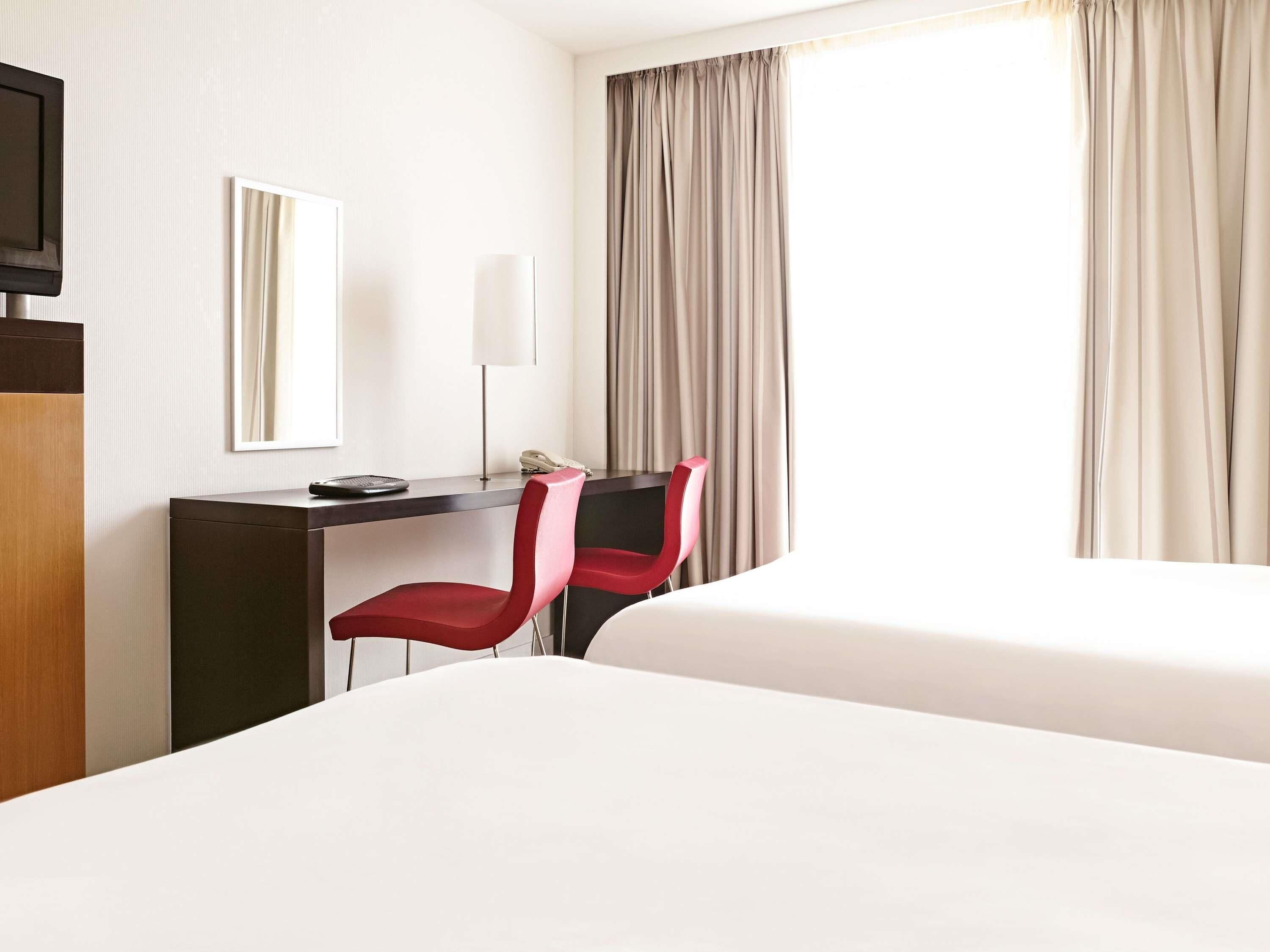 Een hotelkamer met een bed, een bureau met stoel, een telefoon en een raam met gordijnen.