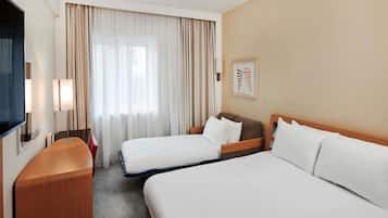 A hotel room with two beds, a TV, a desk, and a window with curtains.