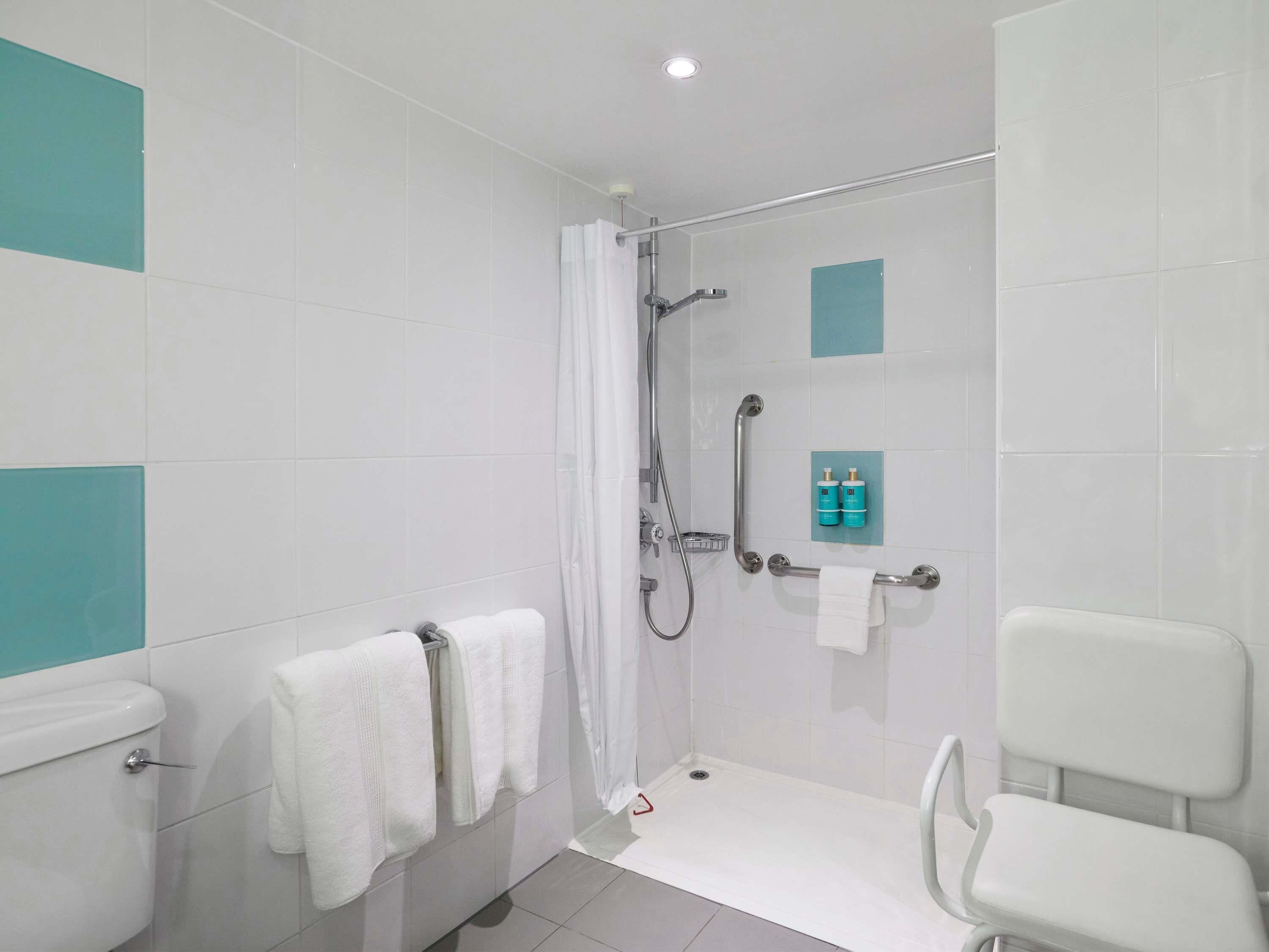 A modern bathroom with a shower, toilet, and a white chair.