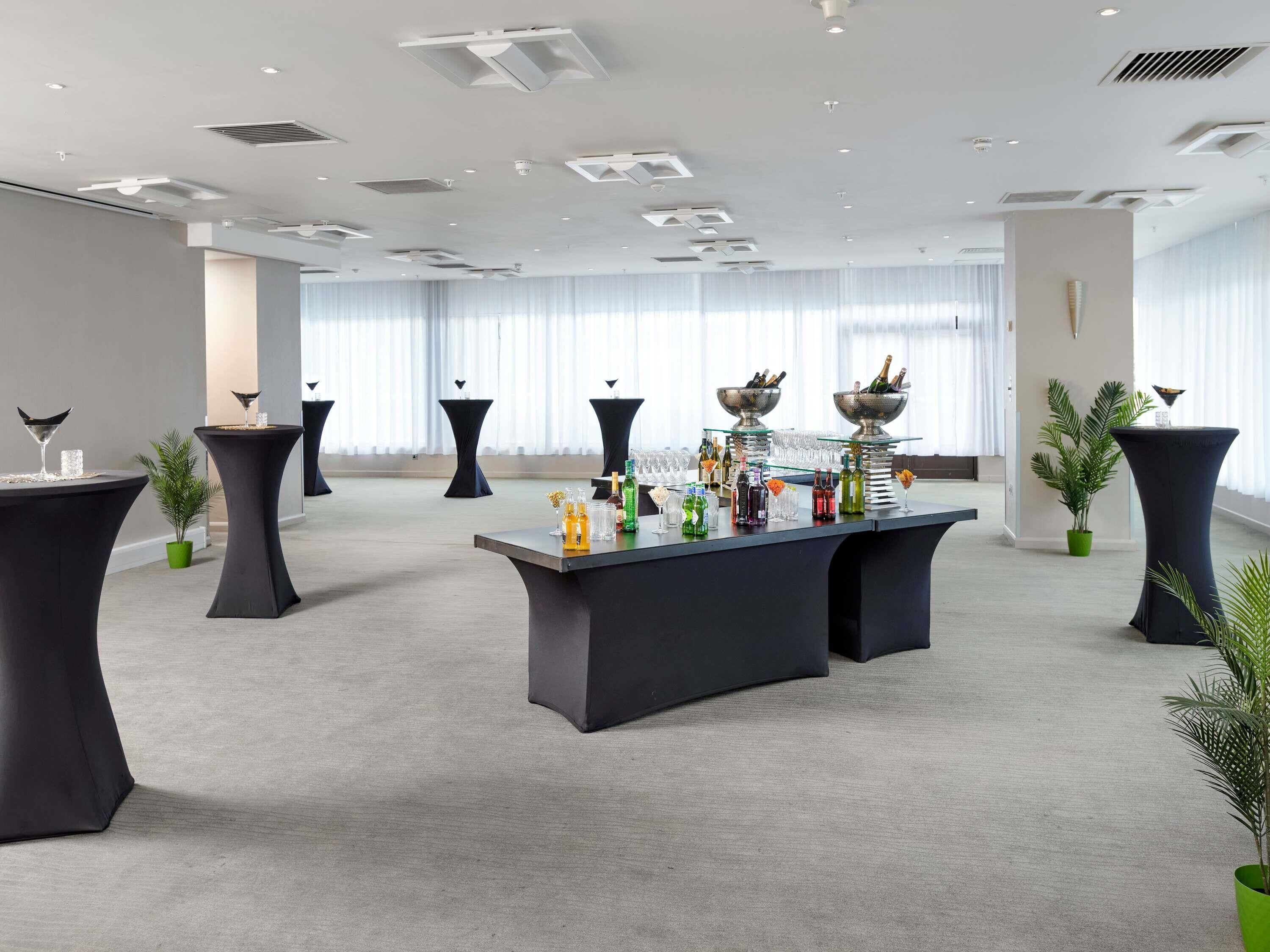 Un salón amplio con barra central, varias mesas y plantas en macetas.