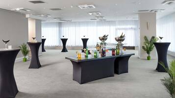 Un salón amplio con barra central, varias mesas y plantas en macetas.