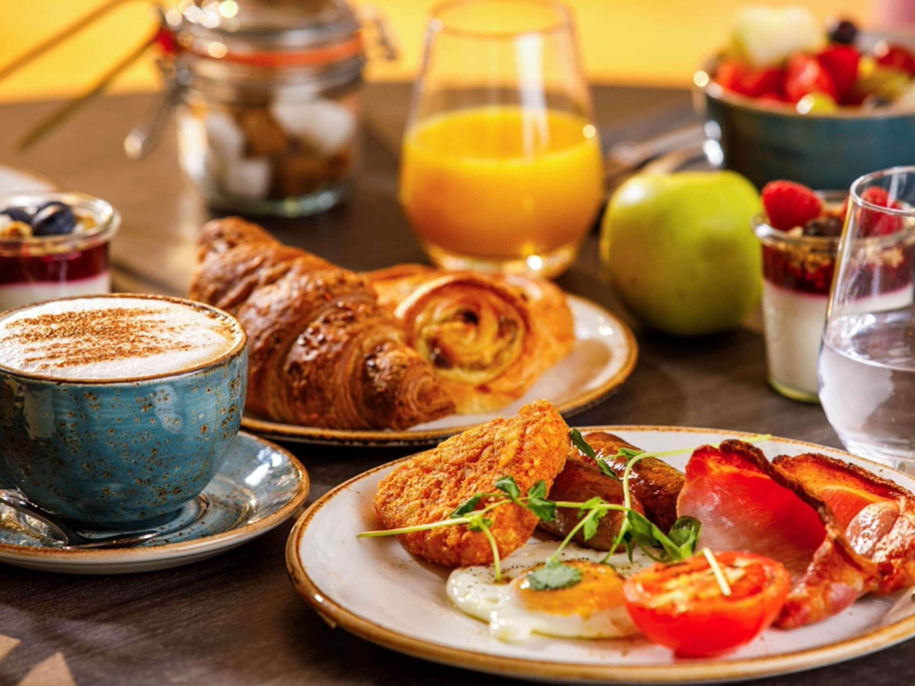 Une table dressée pour le petit-déjeuner avec des croissants, des œufs, des tomates et un verre de jus d’orange.