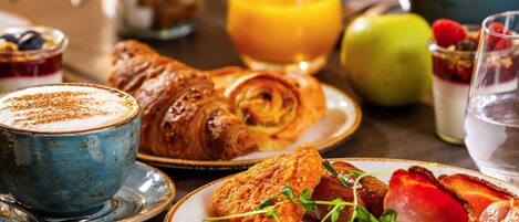 Ein Frühstückstisch mit Croissants, Eiern, Tomaten und einem Glas Orangensaft.