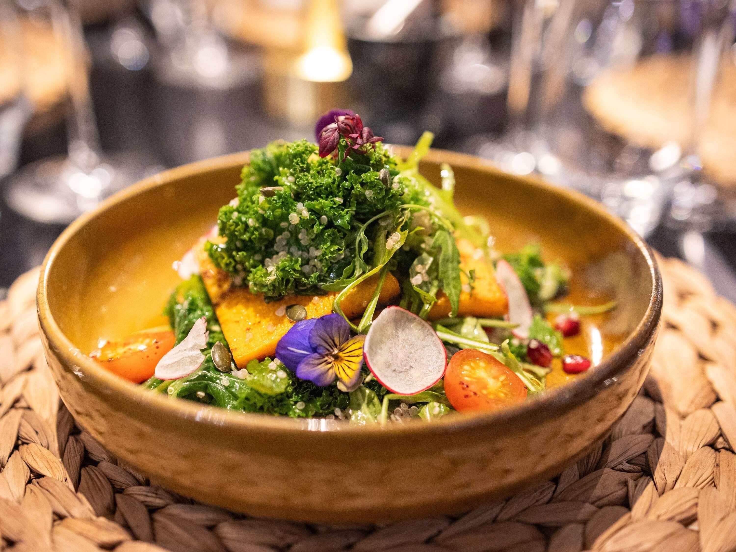 Un tazón de comida con diversas verduras y semillas.