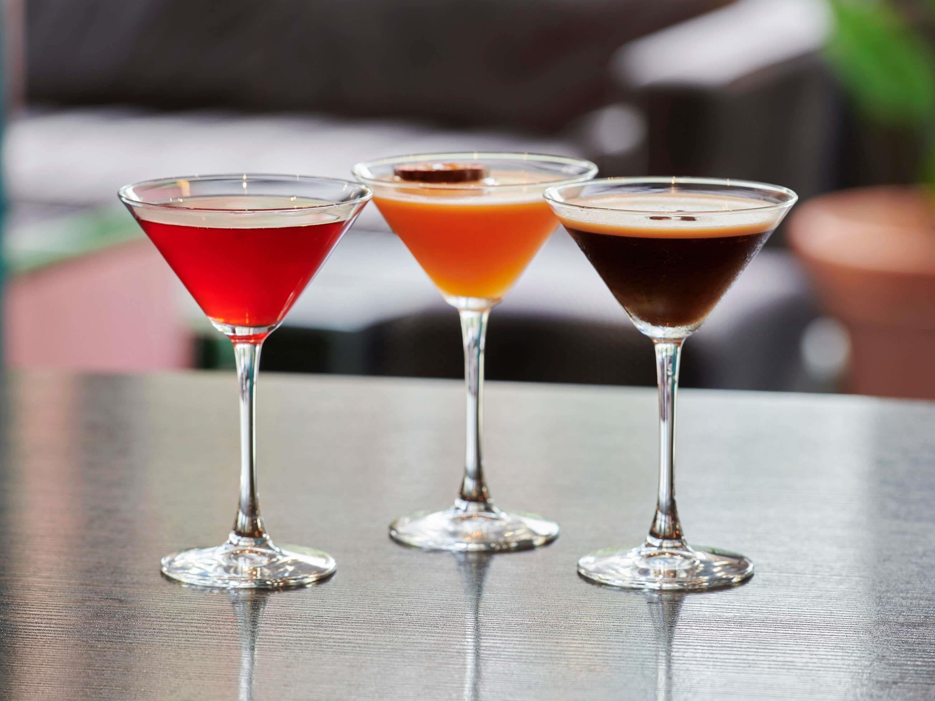 Three martini glasses with different colored drinks on a table.