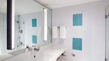 A bathroom with a large mirror, a white sink, a glass shower enclosure, and white tiles with blue accents.