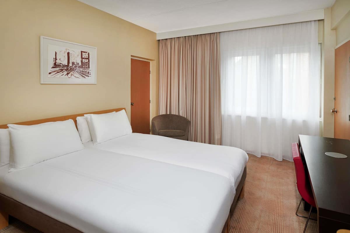 Une chambre dâhĂŽtel avec un grand lit, une chaise, un bureau et une fenĂȘtre avec des rideaux.