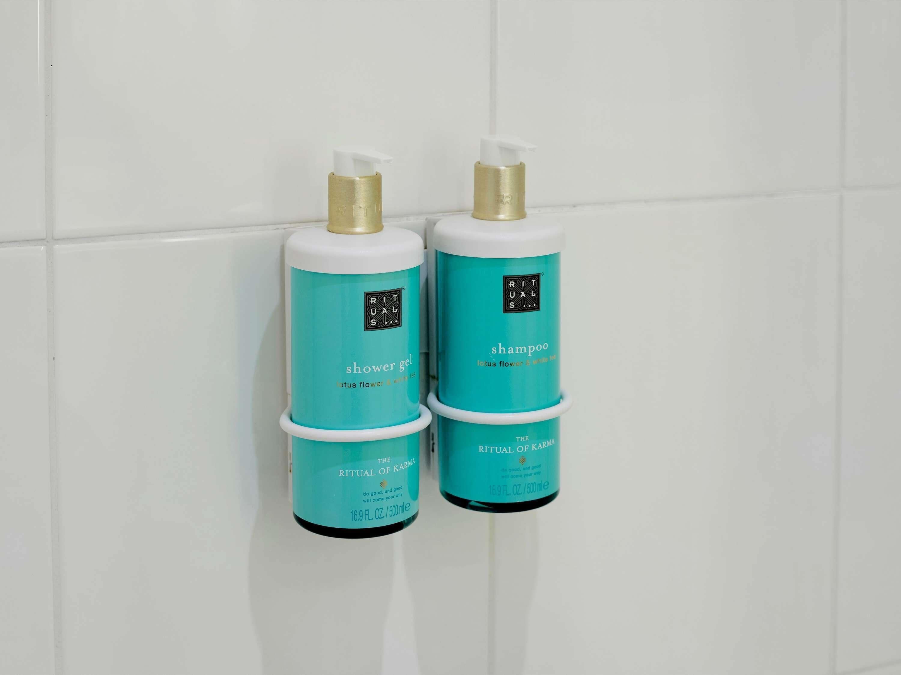 Zwei Flaschen 'Rituals' Shampoo und Duschgel auf einer weißen Fliesenwand.