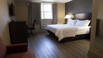 A hotel room with a bed, a desk, a chair, a TV, and a window with curtains.