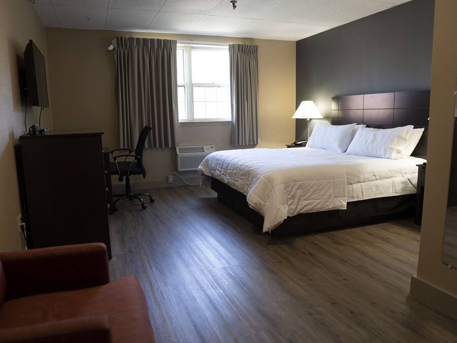 A hotel room with a bed, a desk, a chair, a TV, and a window with curtains.