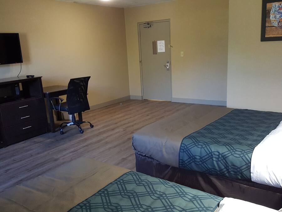 Habitación de hotel con dos camas, un escritorio con silla, televisor y una puerta.
