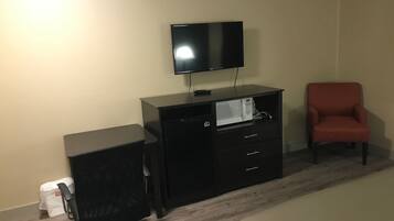 A hotel room with a bed, a desk with a computer, a TV, a microwave, and a red chair.