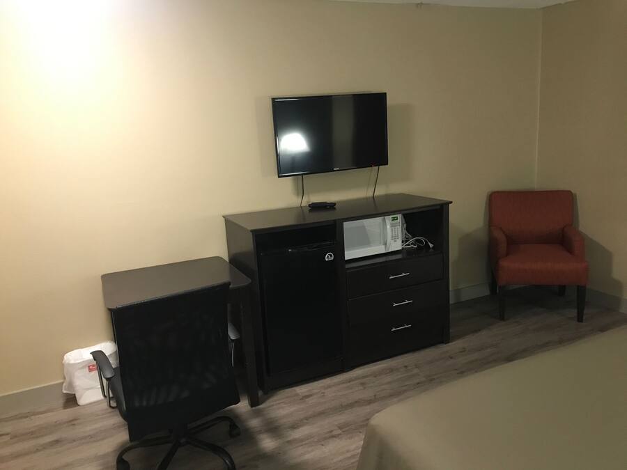 A hotel room with a bed, a desk with a computer, a TV, a microwave, and a red chair.