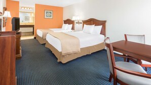 Habitación de hotel con dos camas, un escritorio, una silla, un televisor y un baño con espejo y lavamanos.