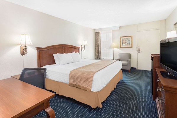 Ein Hotelzimmer mit einem großen Bett, einem Schreibtisch, einem Sessel, einem Fernseher und einem Fenster mit Vorhängen.