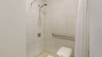 A small, tiled shower area with a grab bar, a white shower seat, and a white curtain.
