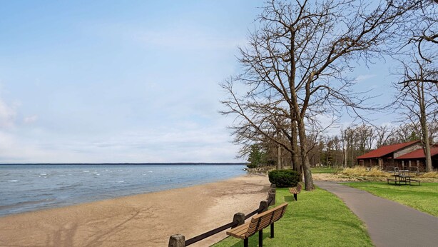 Ein Strand mit einer Holzlattenveranda, einer Bank und einem Weg zu einem Gebäude mit rotem Dach.