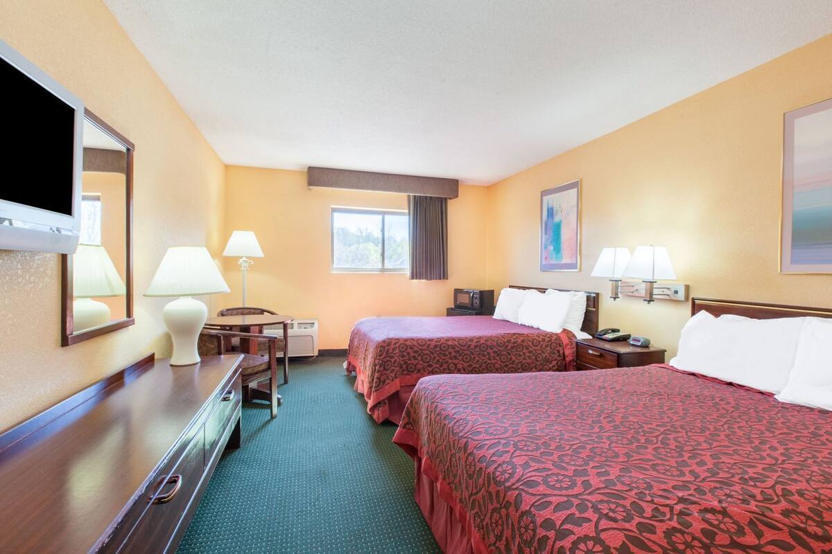 A hotel room with two beds, a desk, a chair, a TV, and a window.