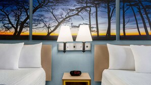 Ein Hotelzimmer mit zwei Betten, einem Nachttisch mit digitaler Uhr, Wandlampen und einem großen Gemälde von Bäumen im Abendrot.