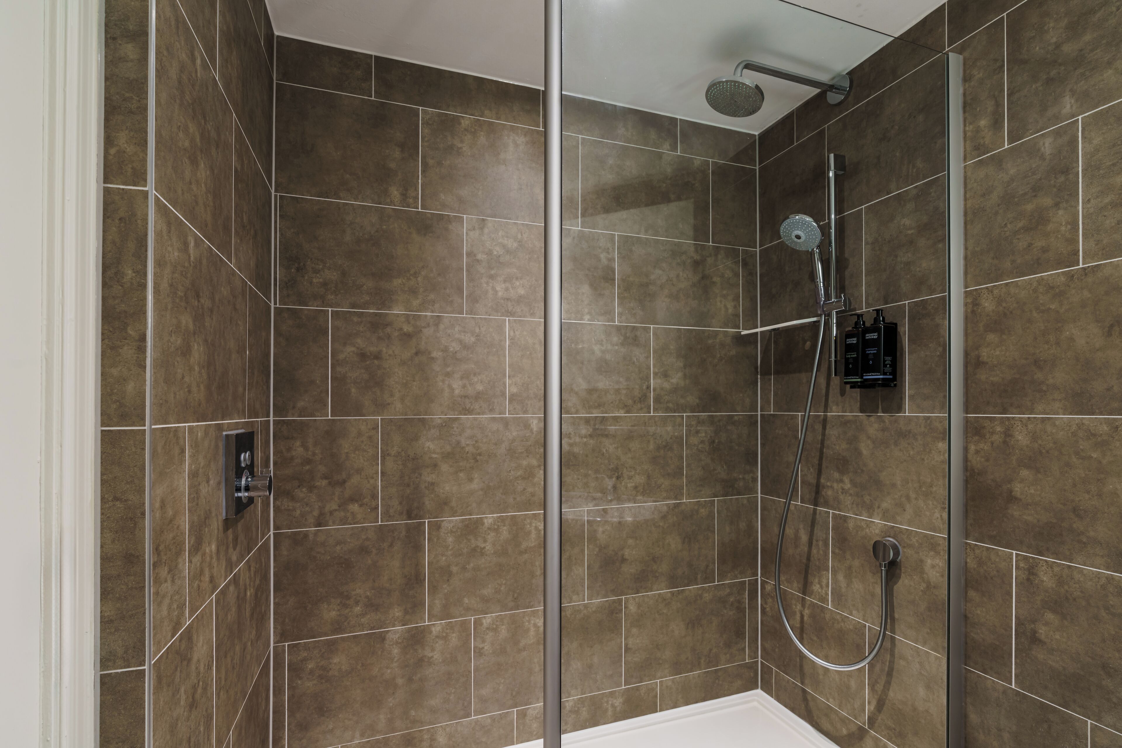 A modern shower area with a glass partition, a handheld showerhead, and a wall-mounted control panel.