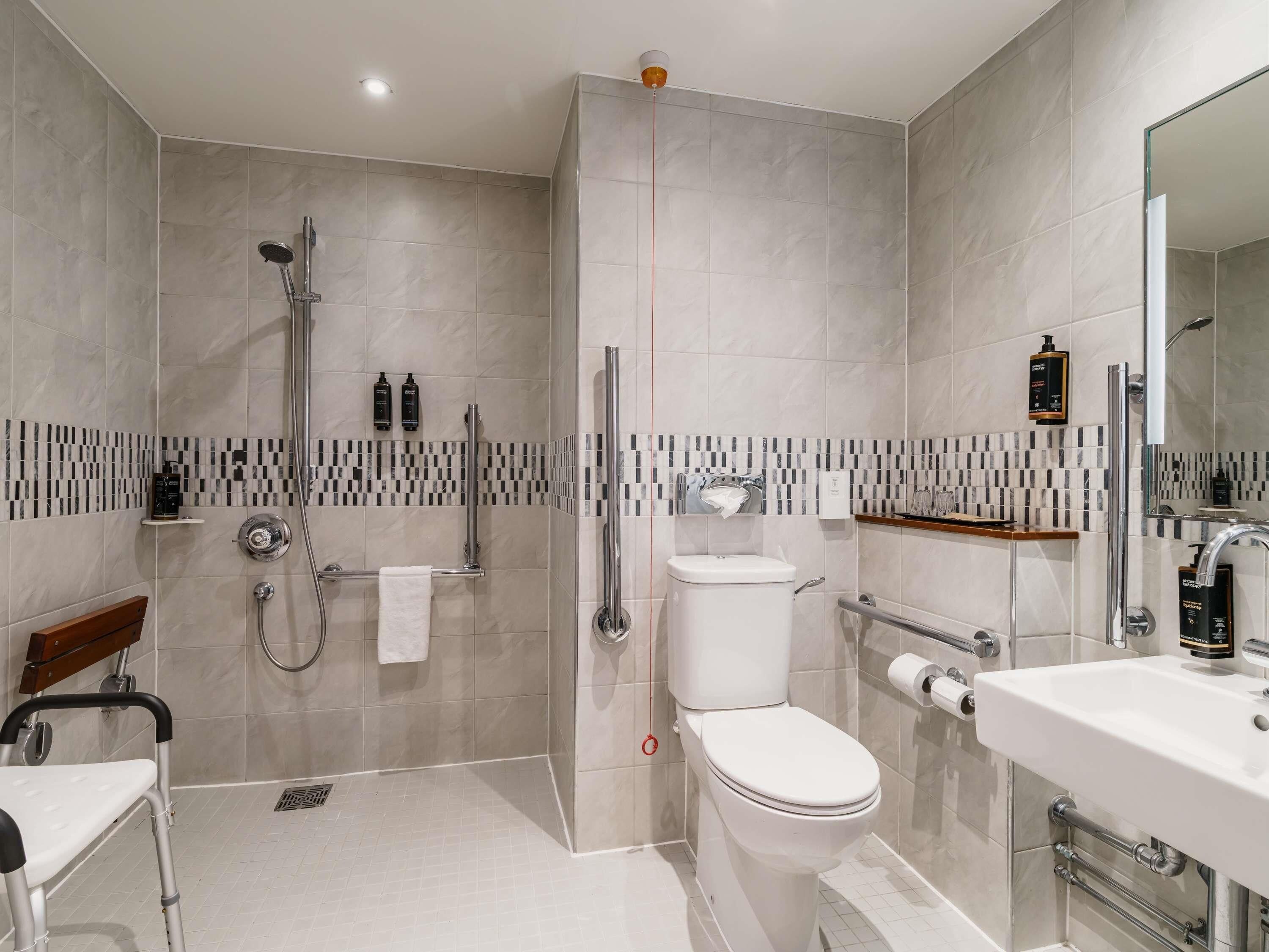 A modern bathroom with a shower, toilet, and sink, featuring a checkered tile backsplash and a wooden bench.