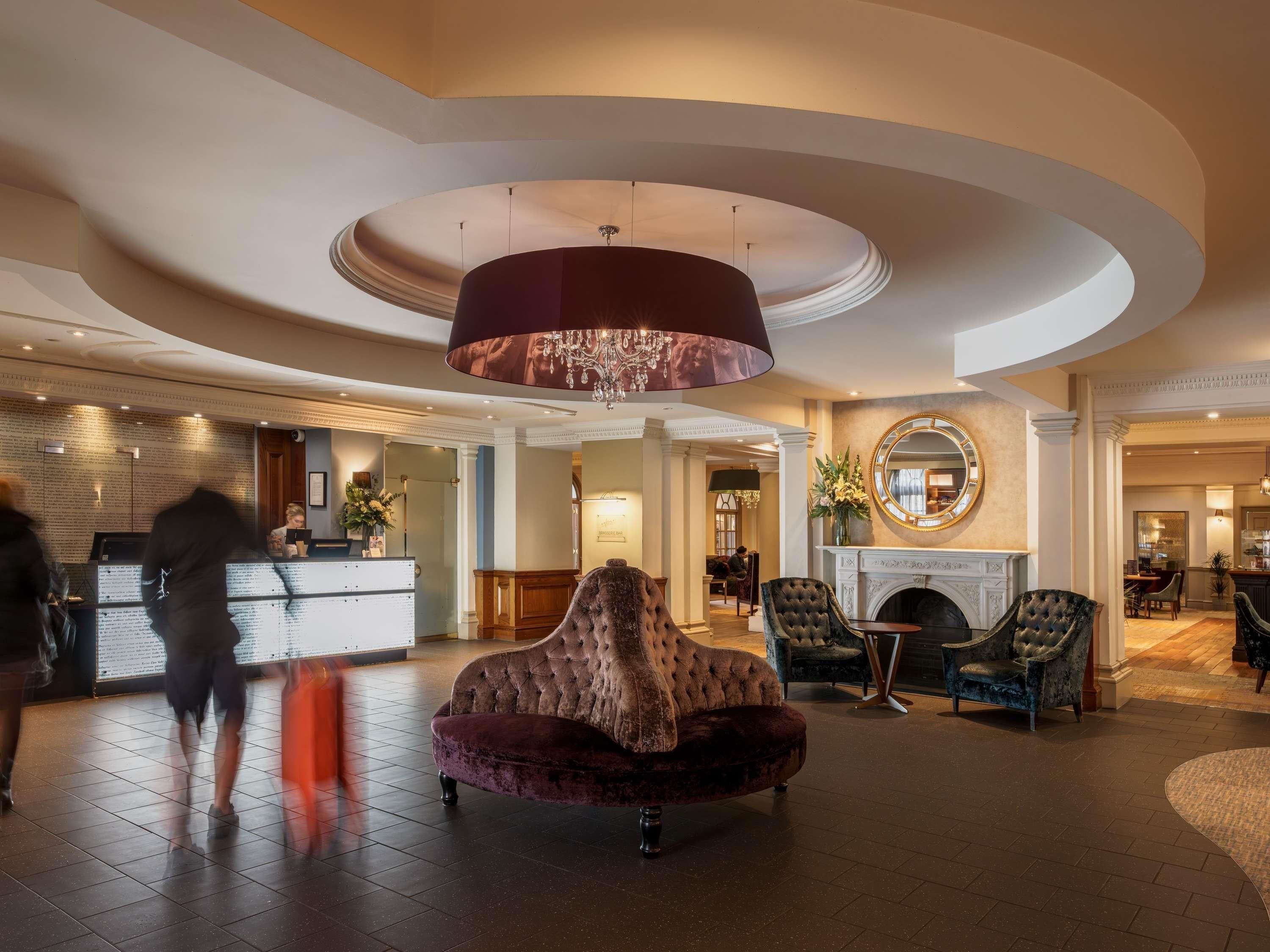 Eine Hotelhalle mit einer Rezeption, einem beeindruckenden Kronleuchter, bequemen Sitzgelegenheiten und einem Kamin.
