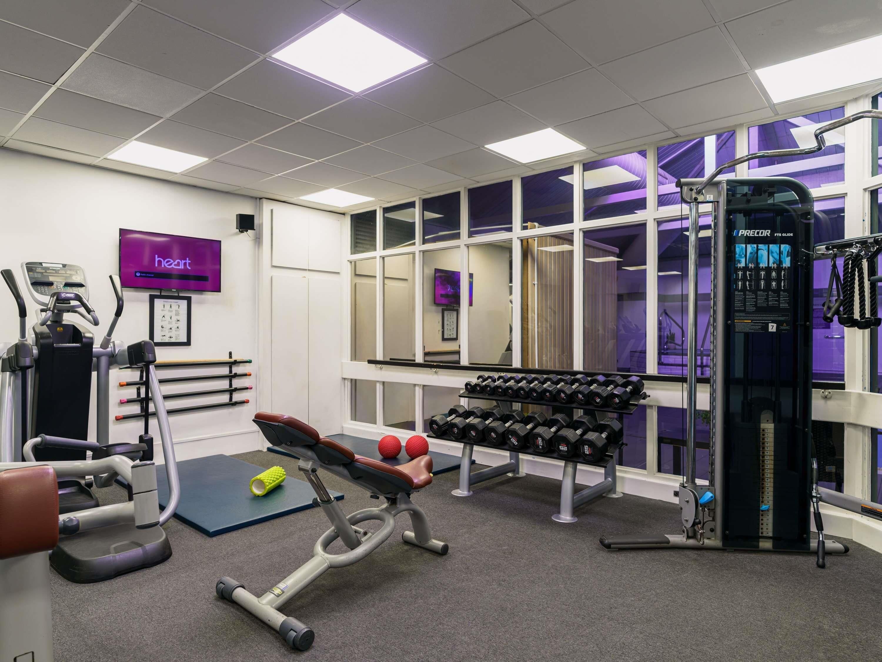 A gym with exercise equipment, a wall-mounted TV, and large windows.