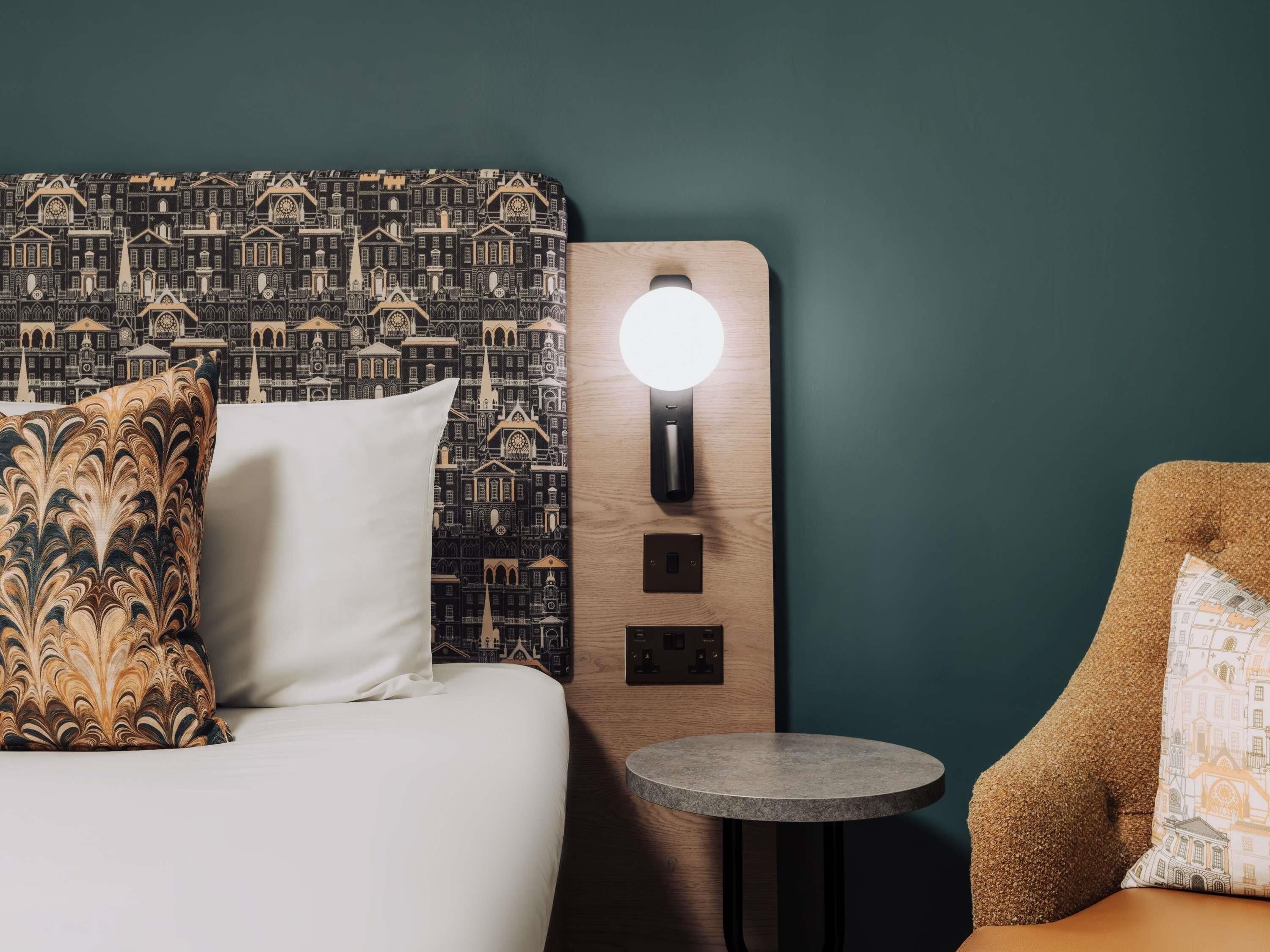 Une chambre d’hôtel avec une tête de lit à motifs, une table de chevet avec une lampe et une petite table ronde.