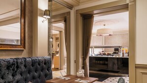 Un vestíbulo de hotel con un sofá negro capitonado, una mesa de madera con un jarrón y saleros y pimenteros, y vistas al área de la cocina.