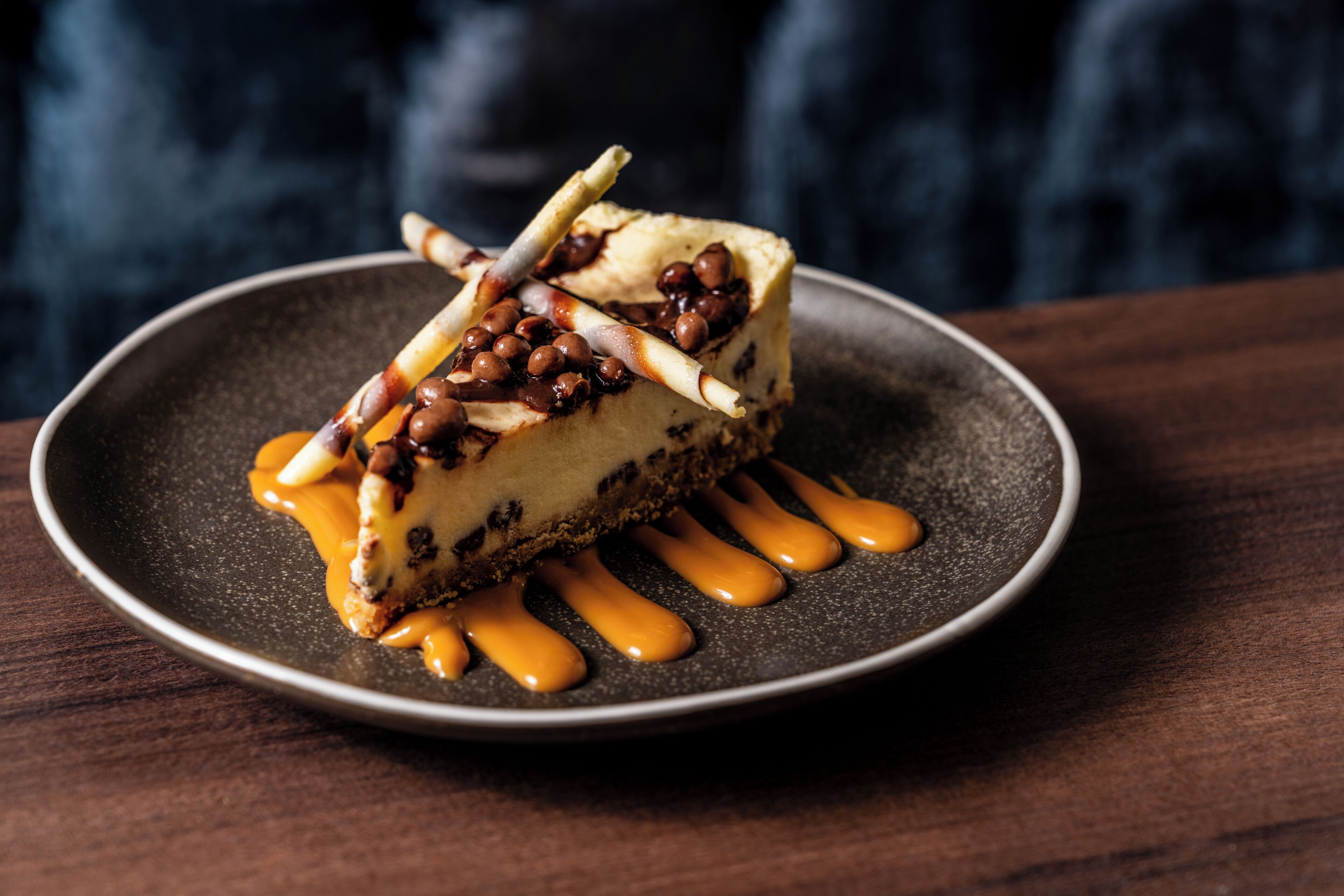 A slice of cheesecake with caramel sauce and nuts on a plate.