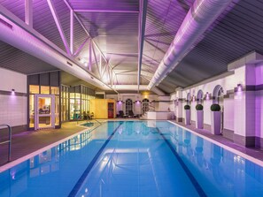 Una piscina interior con suelo de baldosas, zona de terraza de madera y mostrador de recepción.