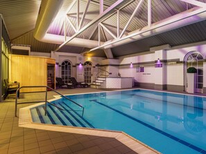 An indoor swimming pool with a clear view of the pool area, a set of stairs leading into the pool, and a lounge area with chairs and a small table. - Mercure Exeter Southgate Hotel (Exeter)
