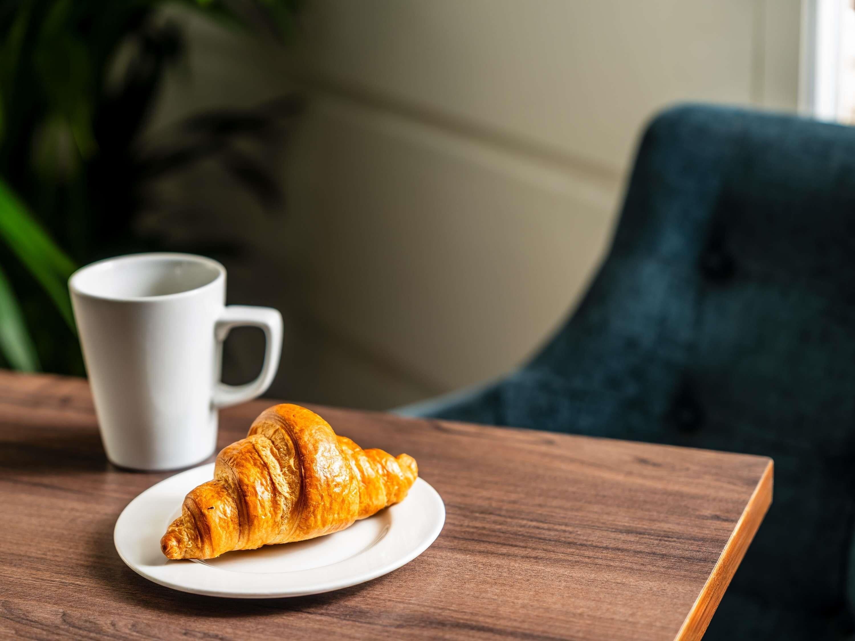A croissant on a white plate with a white cup in the background.