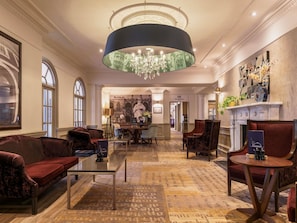 Um hall de hotel com um candelabro, área de estar, lareira e uma pintura grande na parede.