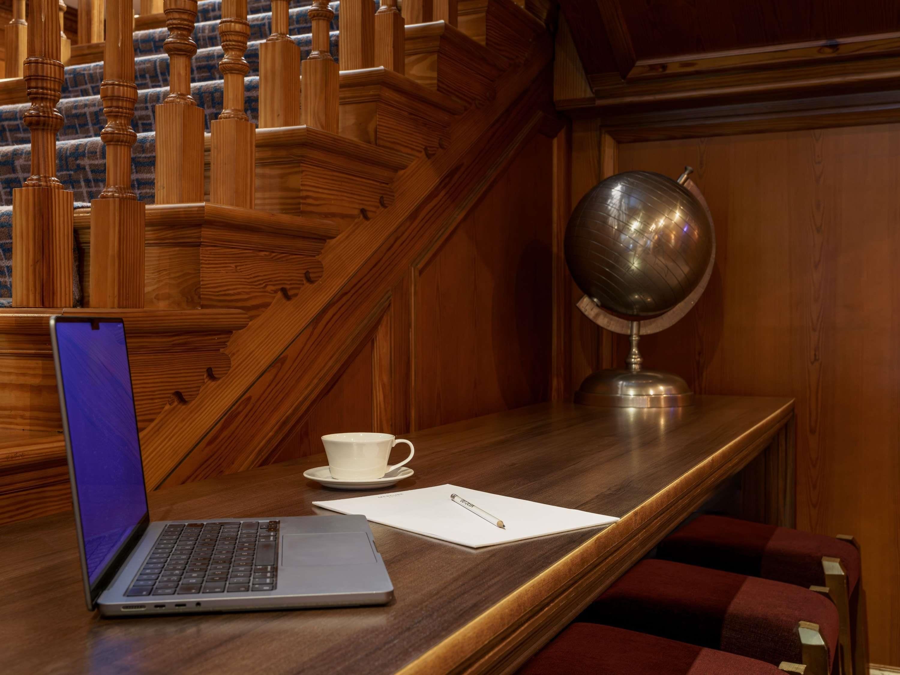 A wooden desk with a laptop, a white cup, a globe, and a notepad.