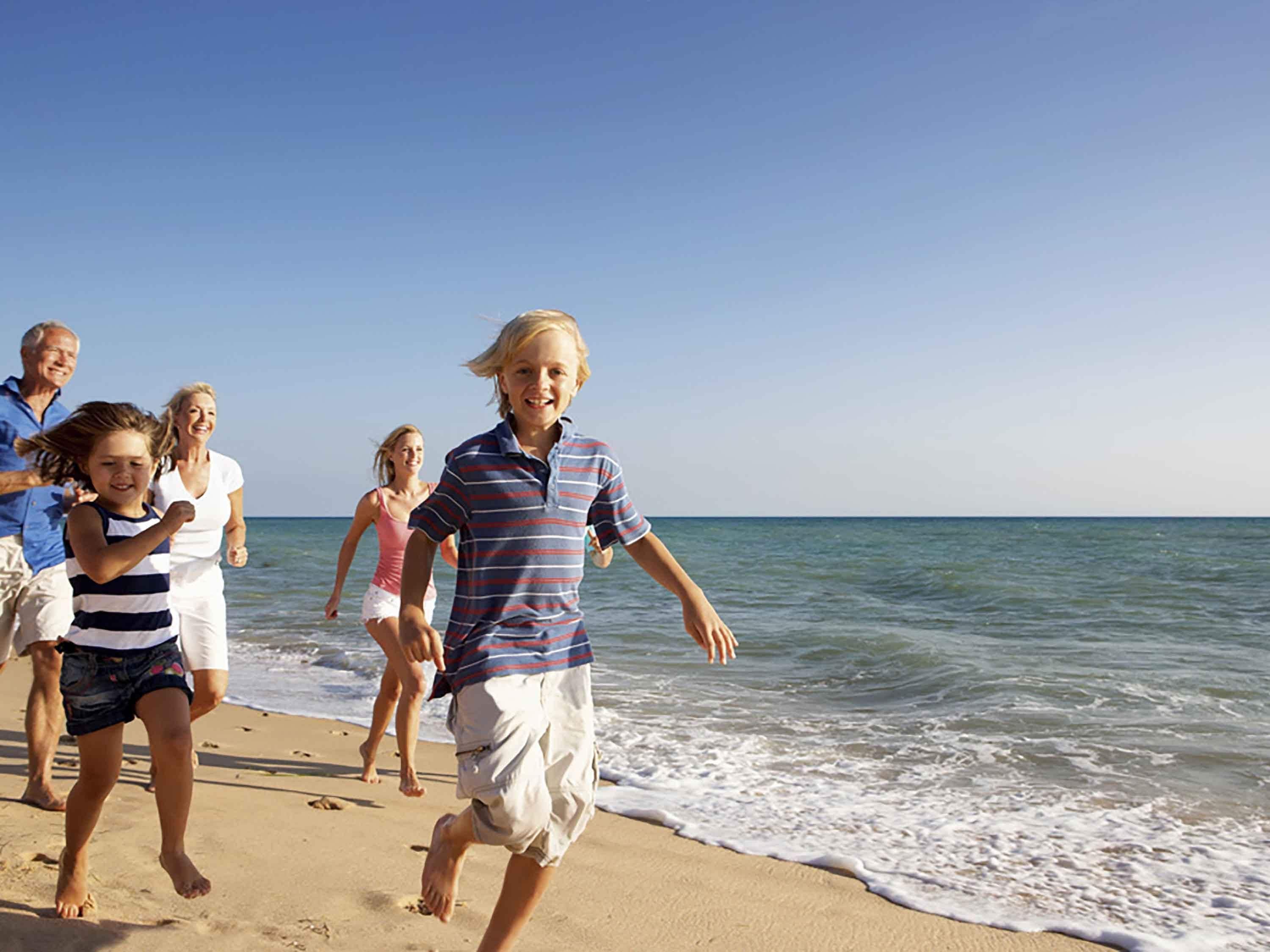 A family running along a sandy beach with the ocean in the background.