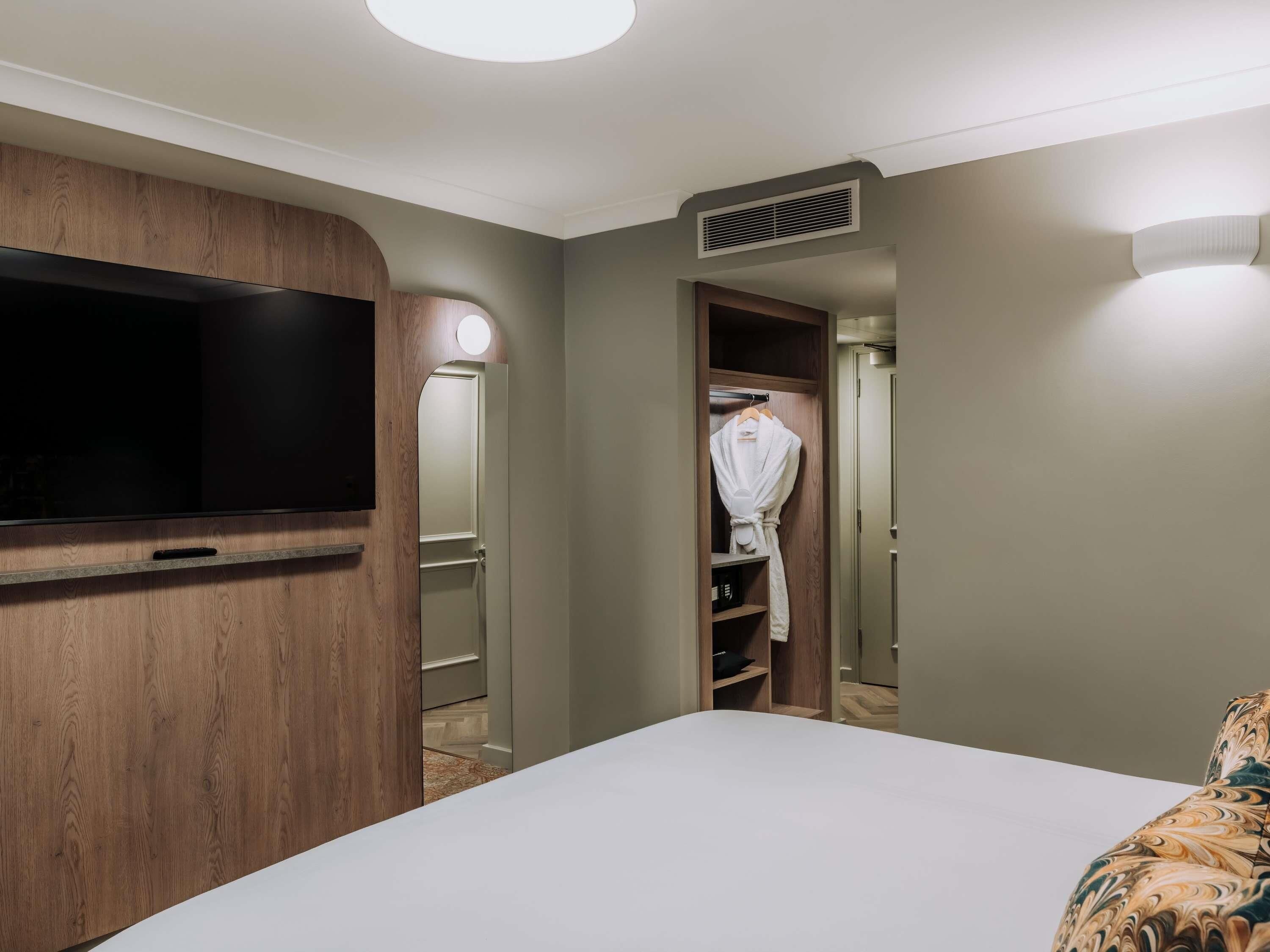A hotel room with a bed, a television, a wardrobe, and a mirror.