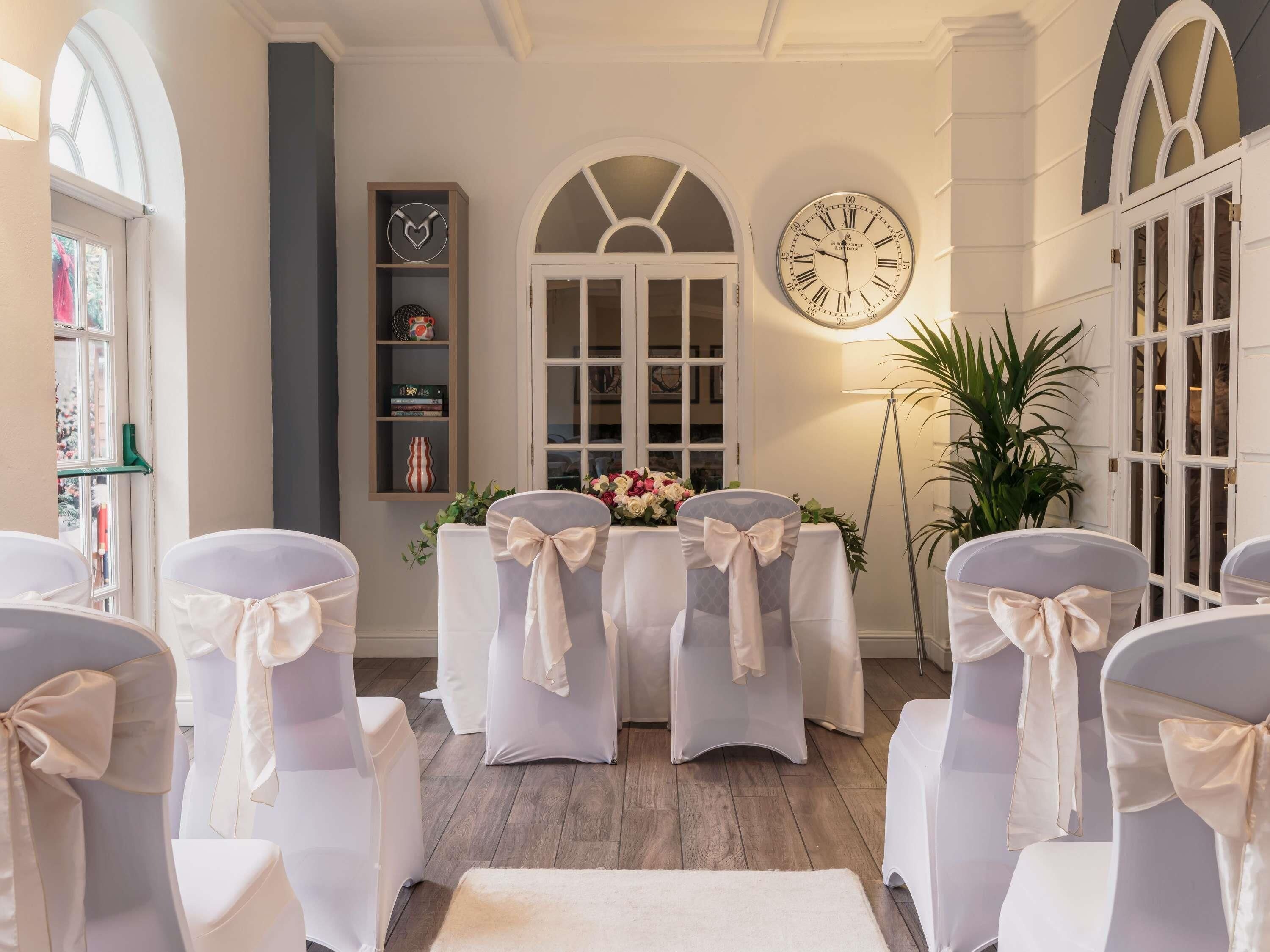 A room with white chairs, a clock, and a table with flowers.