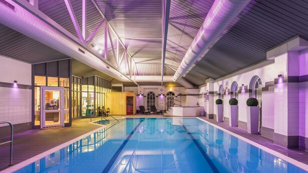 Una piscina interior con suelo de baldosas, zona de terraza de madera y mostrador de recepción.