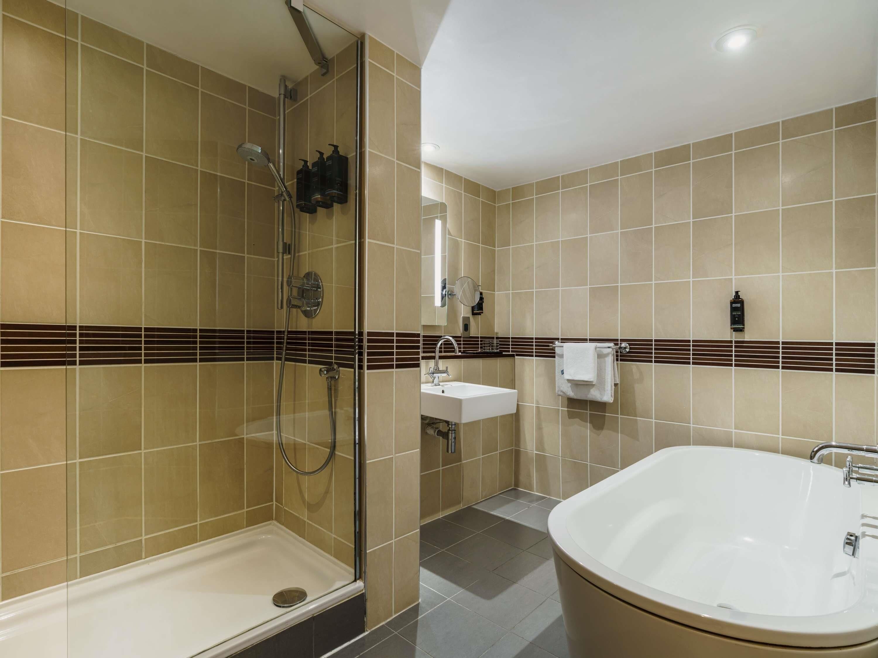 Un baño moderno con ducha a ras de suelo, una bañera independiente, un lavabo y un perchero para toallas.