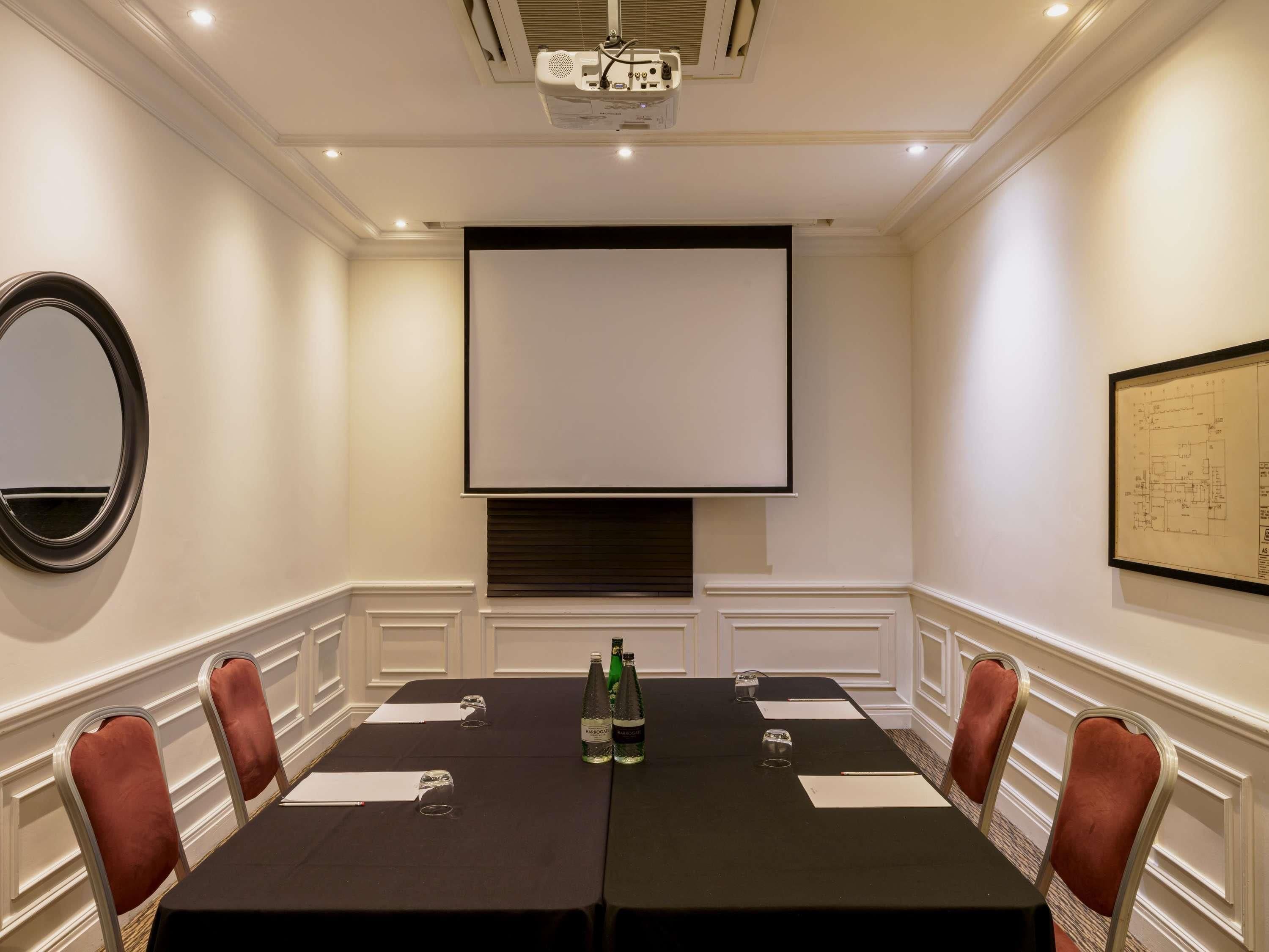 Ein Konferenzraum mit Projektionsschirm, einem Tisch mit Stühlen und einem an der Decke befestigten Projektor.
