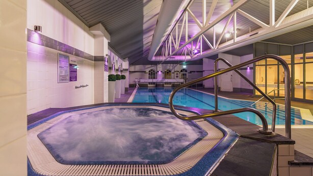 Un espace dédié aux bains à remous, comprenant une piscine, des garde-corps en métal et un plafond avec des poutres apparentes.