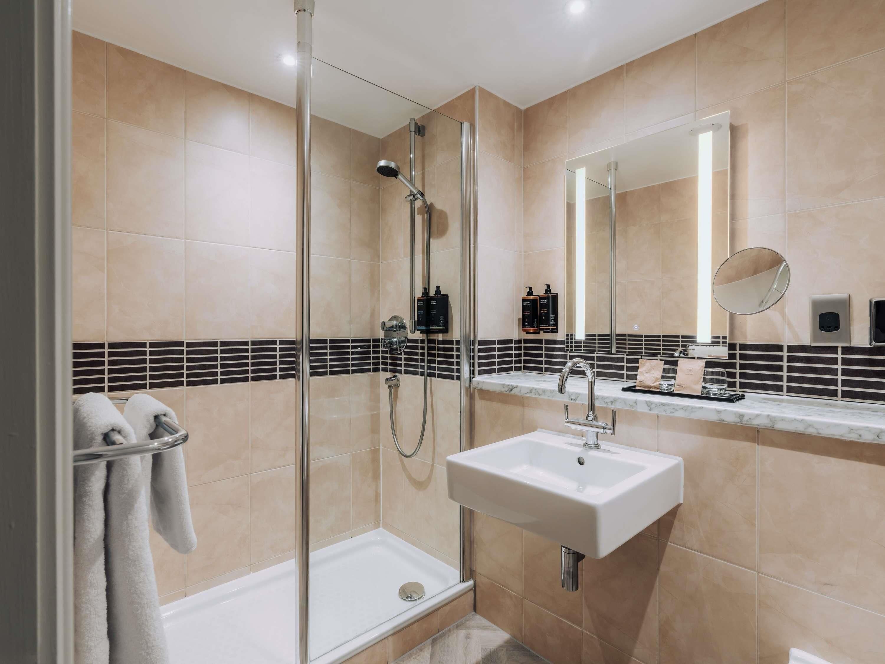 Un baño moderno con ducha de vidrio, un lavamanos blanco y un espejo grande.