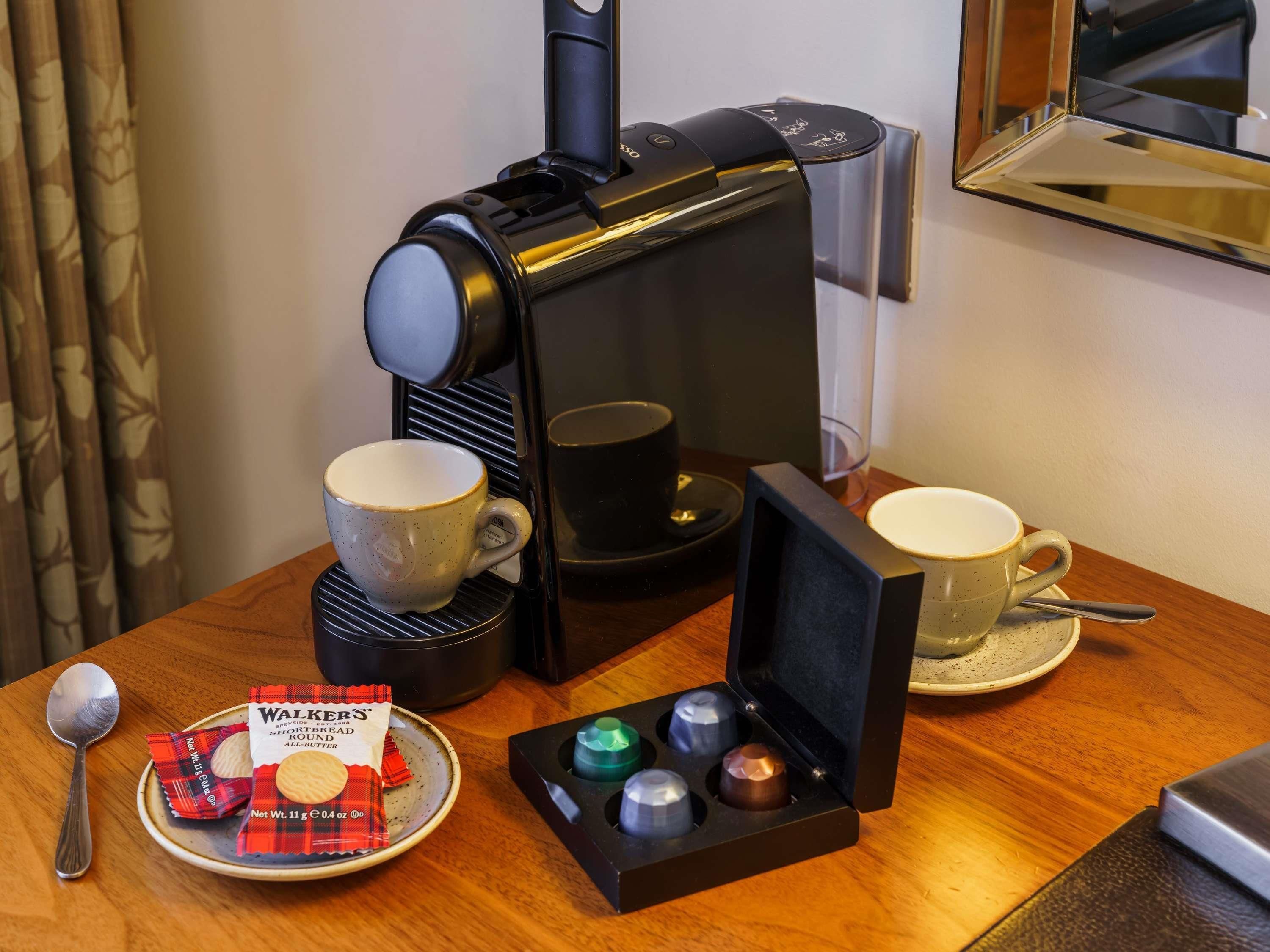 Une machine à café, deux tasses, une assiette avec des biscuits, une cuillère et une boîte de biscuits Walkers sur une table en bois.