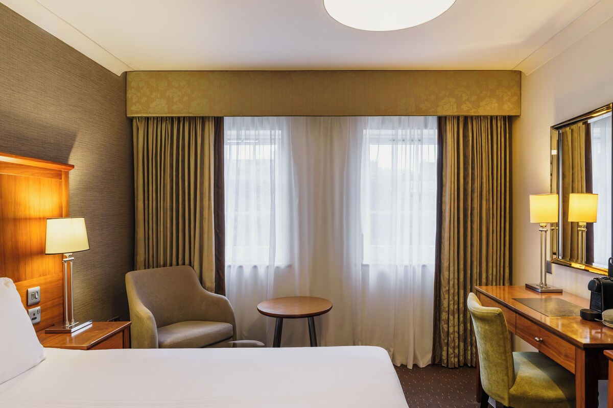 Una habitación de hotel con cama, escritorio, silla, mesita y espejo.