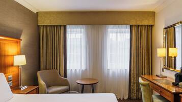 A hotel room with a bed, a desk, a chair, a small table, and a mirror.