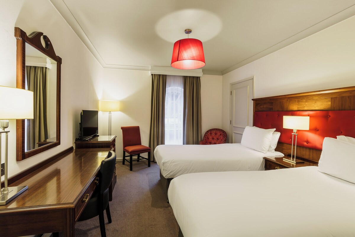 Habitación de hotel con dos camas, un escritorio, una silla, un televisor y una lámpara colgante roja.